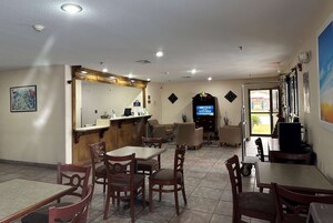 Um hall de hotel com balcão de recepção, área de estar e uma tela de televisão.