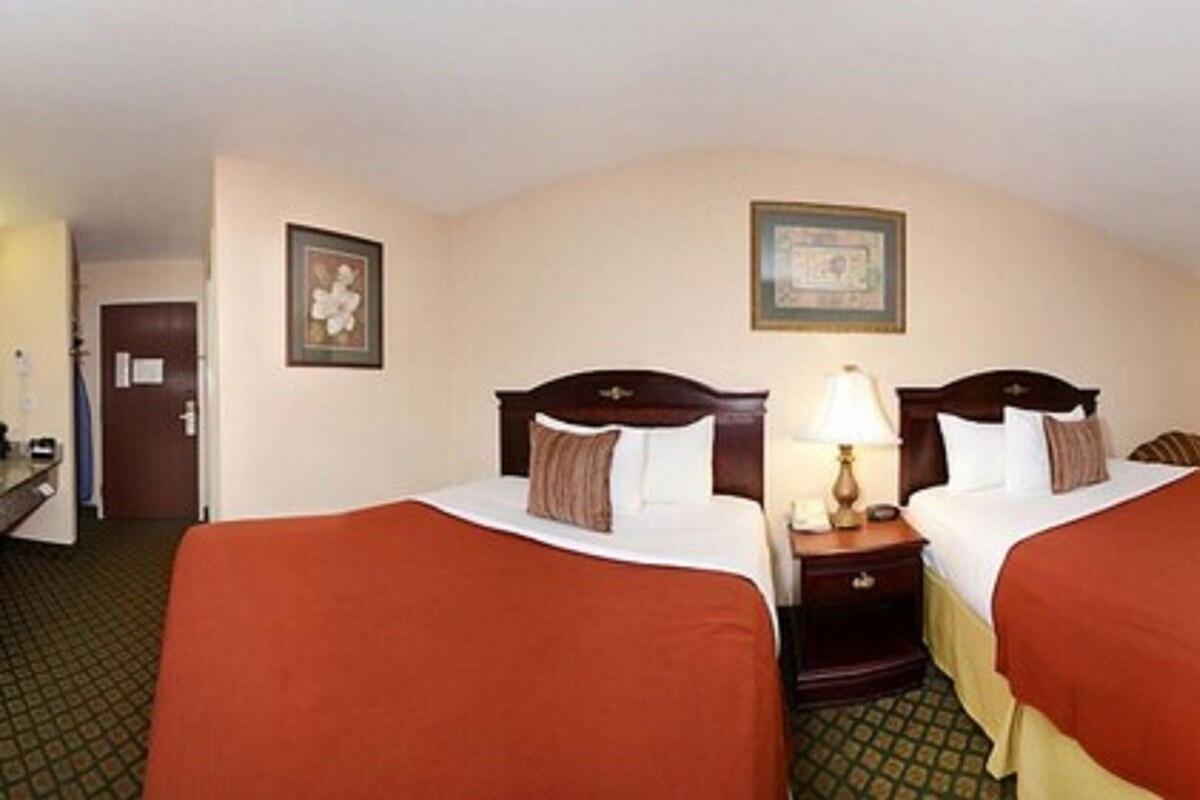 A hotel room with two beds, a nightstand with a lamp, a framed picture on the wall, and a door.
