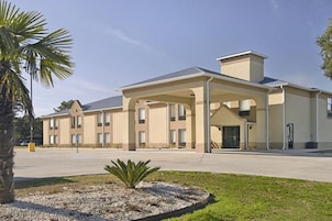 Um hotel moderno com entrada coberta, vários andares e um jardim frontal bem cuidado.