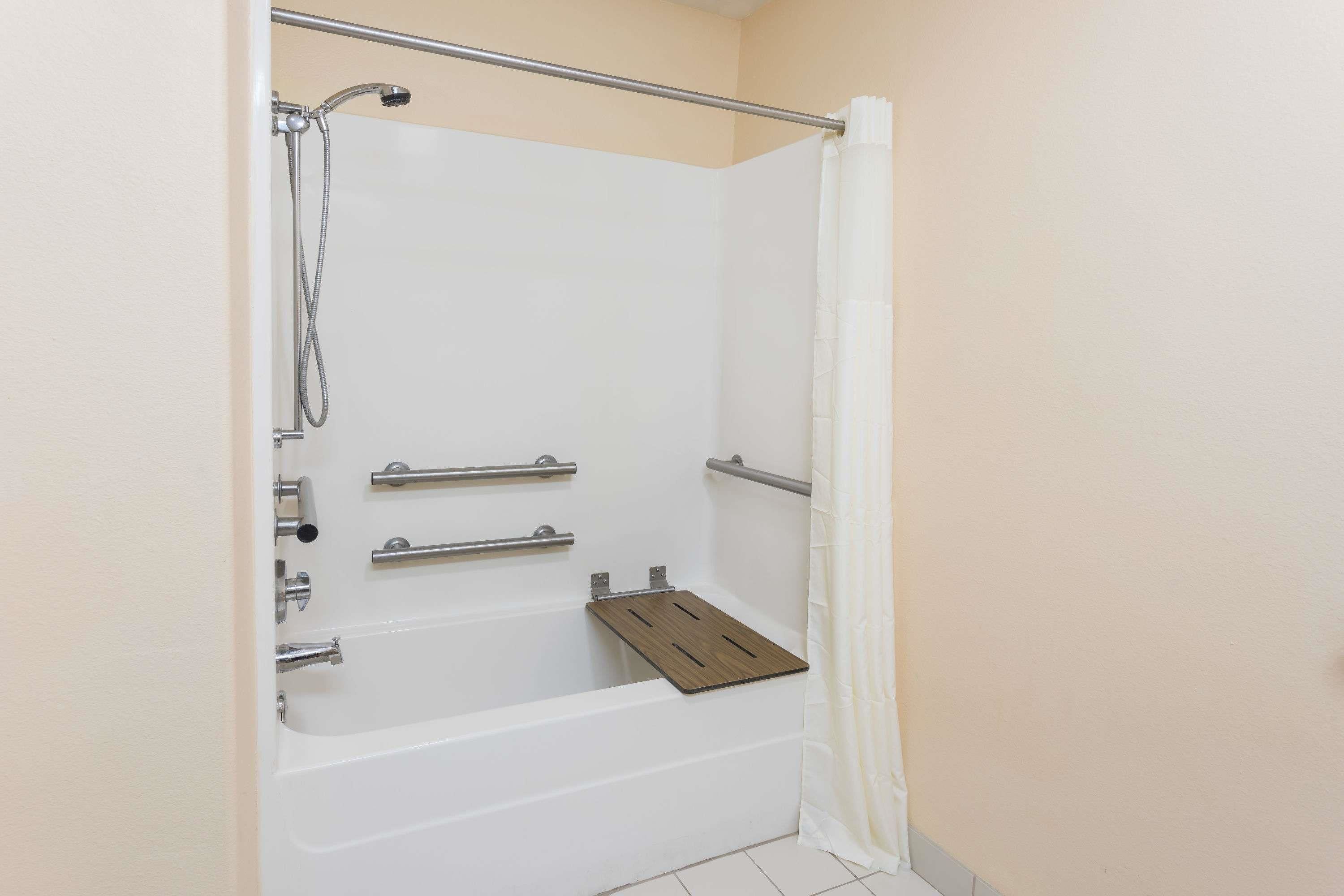 A walk-in shower with a grab bar, a showerhead, and a wooden shelf.