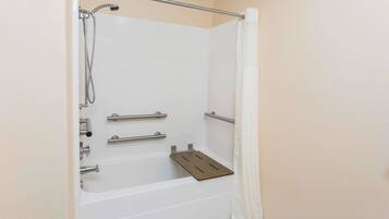 A walk-in shower with a grab bar, a showerhead, and a wooden shelf.