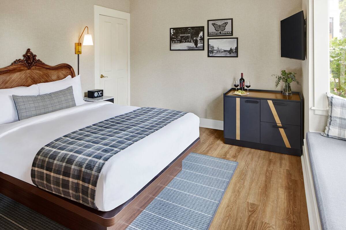 Habitació d'hotel amb un llit gran, una taula de nit, una làmpada i un armari amb mirall. Hi ha dos quadres amb marc a la paret i un televisor muntat a la paret.