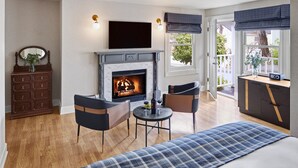 A cozy room with a fireplace, a TV, a dining area, and a view of the outdoors. - Gosby House Inn, A Four Sisters Inn (Pacific Grove)