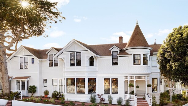 A large, white Victorian-style house with multiple windows, a prominent turret, and a well-maintained garden. - Gosby House Inn, A Four Sisters Inn (Pacific Grove)