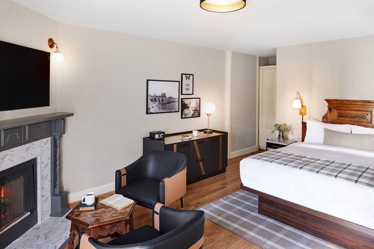 Habitació d'hotel amb una xemeneia, un llit, un escriptori amb una làmpada i una cadira.