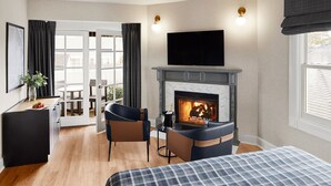 Une chambre d’hôtel avec une cheminée, un lit, un bureau avec une chaise et une vue sur l’extérieur, visible à travers une porte vitrée.