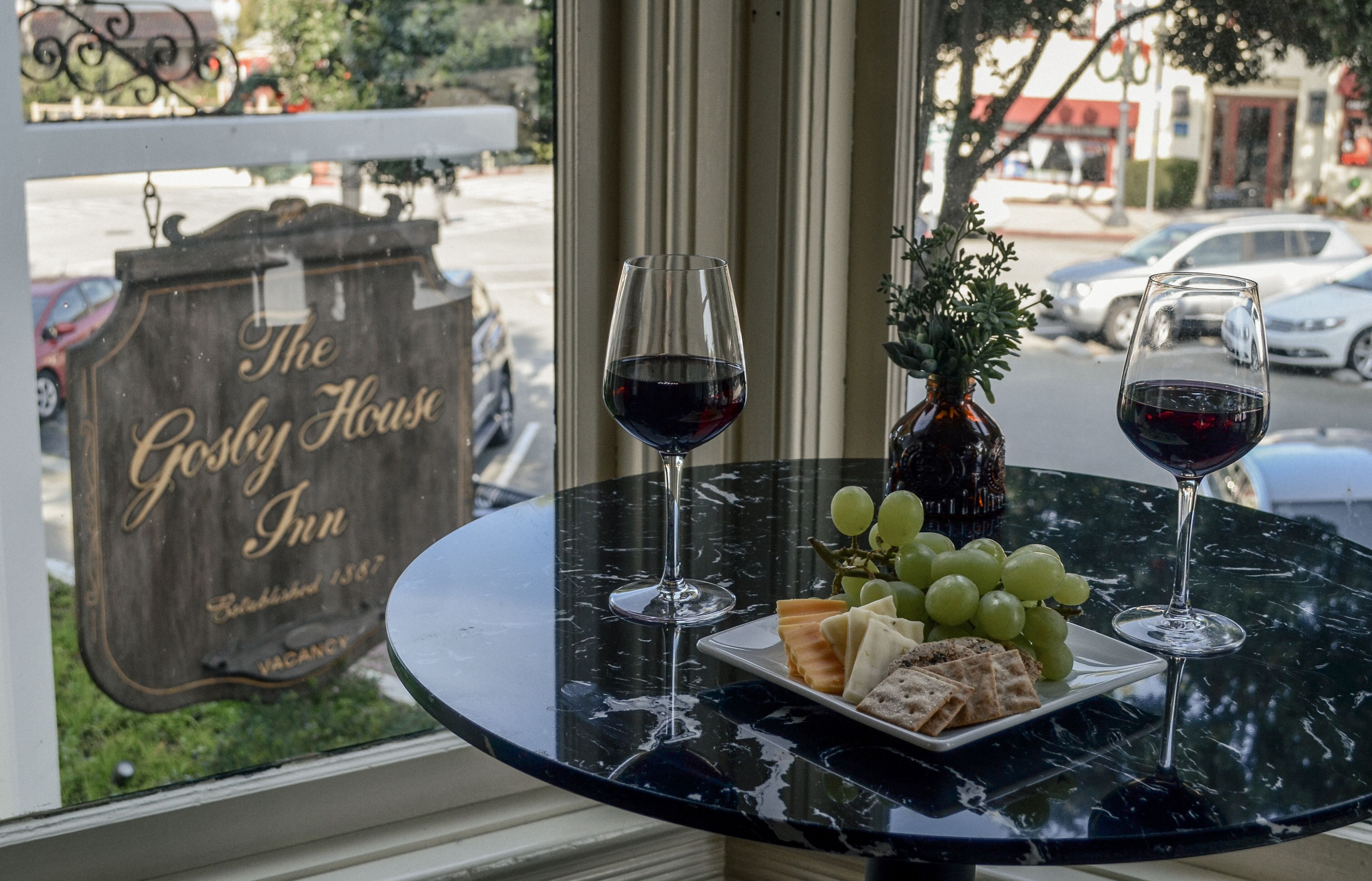 A table with two wine glasses, a plate of cheese and crackers, and a vase with green grapes.