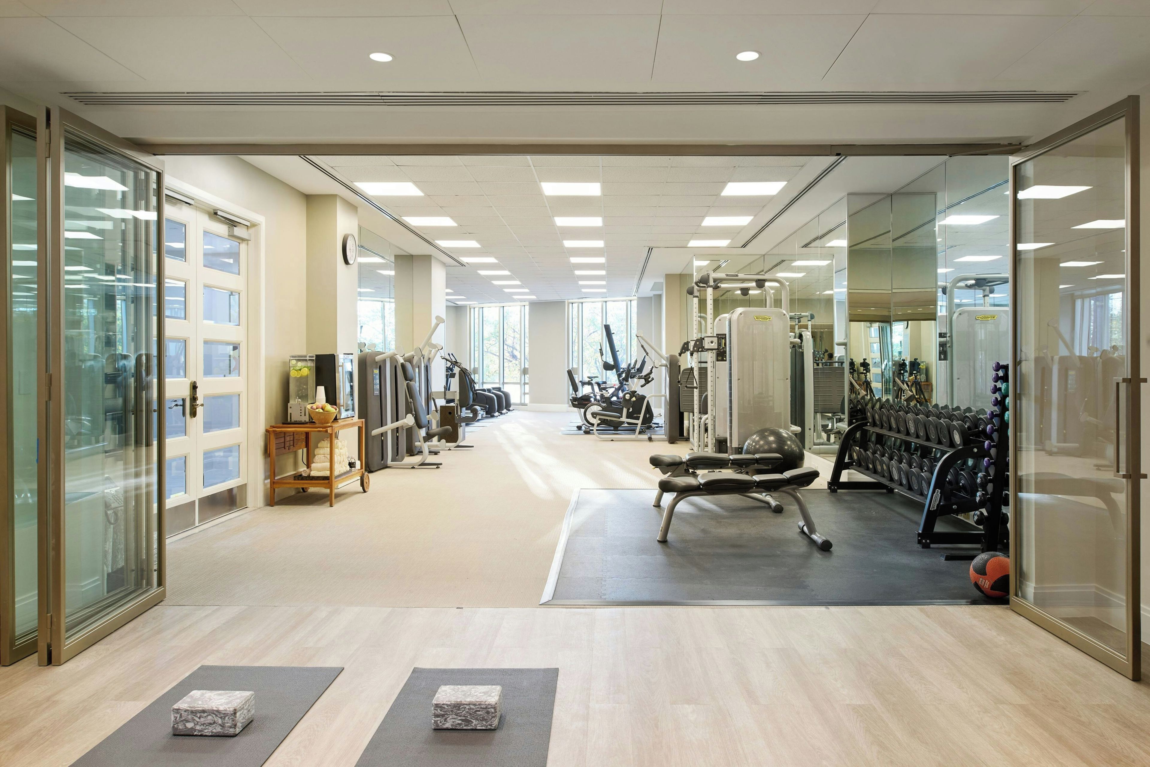 Un gimnasio con equipo de ejercicio, un espejo y una mesa de madera con un frutero.
