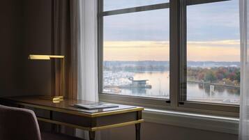 A modern room with a desk, a chair, and a large window offering a view of a cityscape and water.