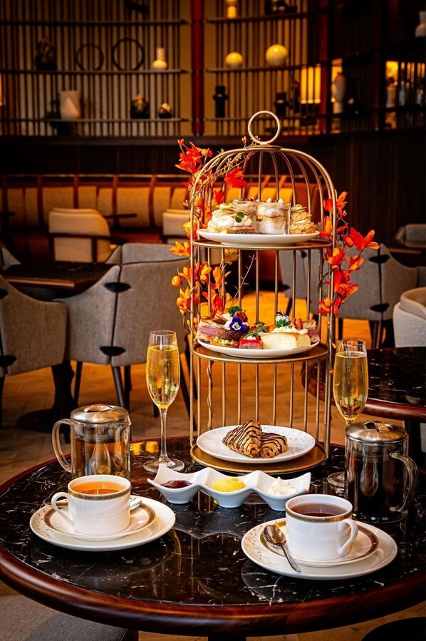 A three-tiered dessert display with floral decorations, a coffee and tea setup, and a wine glass on a table in a restaurant setting. - The Potomac Hotel, Autograph Collection (Washington)