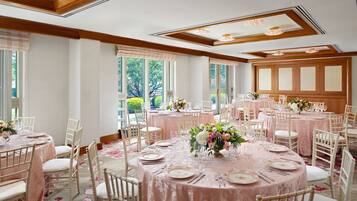 A spacious room with multiple round tables, each set with white chairs, plates, and cutlery.