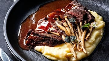 A plate of steak with mushrooms and sauce, served on a black plate with a fork and knife beside it.