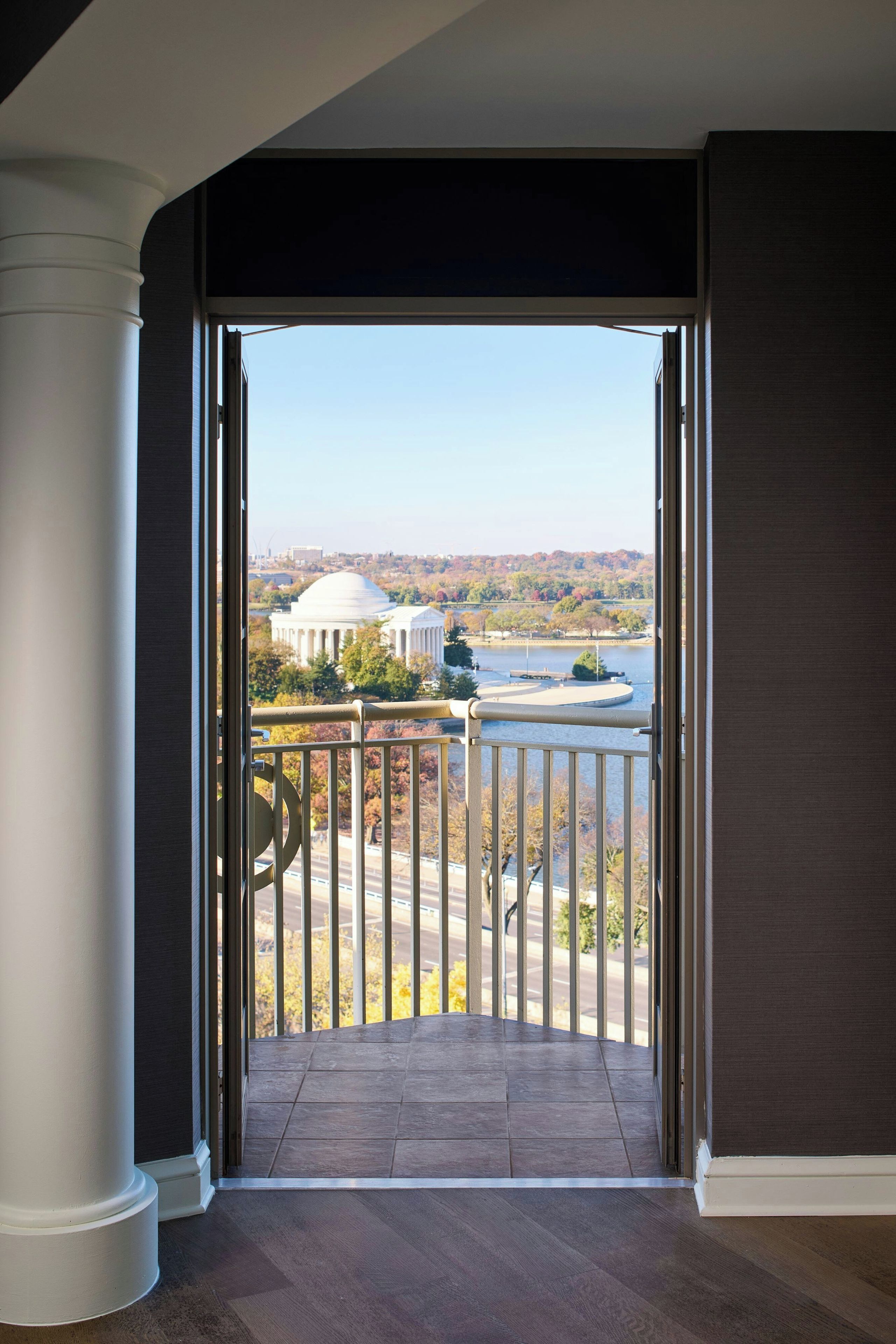 A view from an open door leading to a balcony with a view of a large building and a body of water.