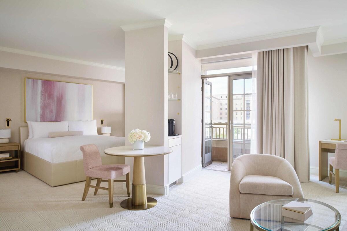 Habitación de hotel con una cama grande, una mesa redonda con una silla, una pequeña mesa redonda con una silla, un sofá y vistas al exterior.