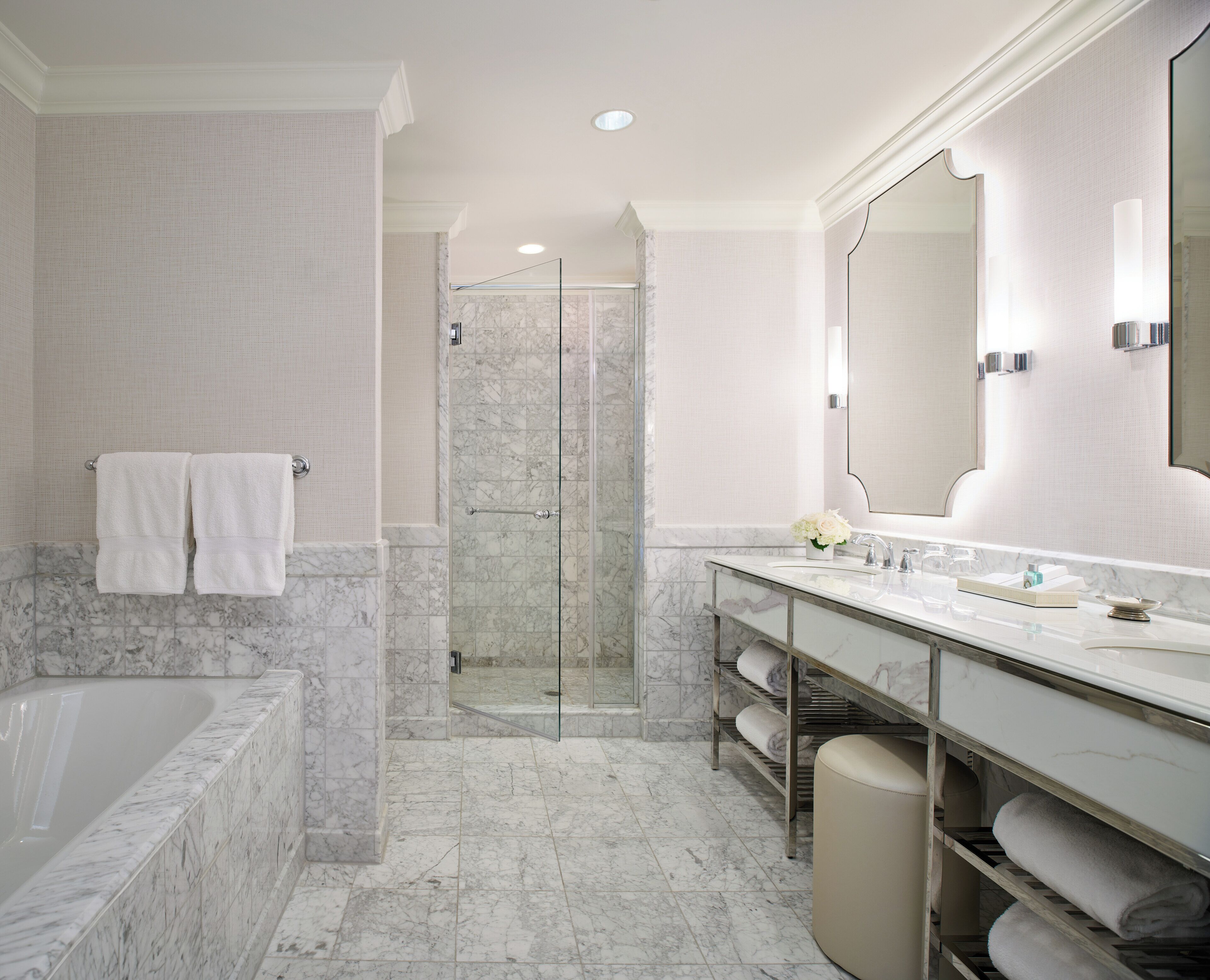 A bathroom with a bathtub, a walk-in shower, a vanity with a large mirror, and marble flooring.