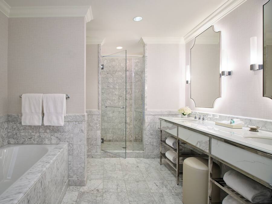 A bathroom with a bathtub, a walk-in shower, a vanity with a large mirror, and marble flooring.