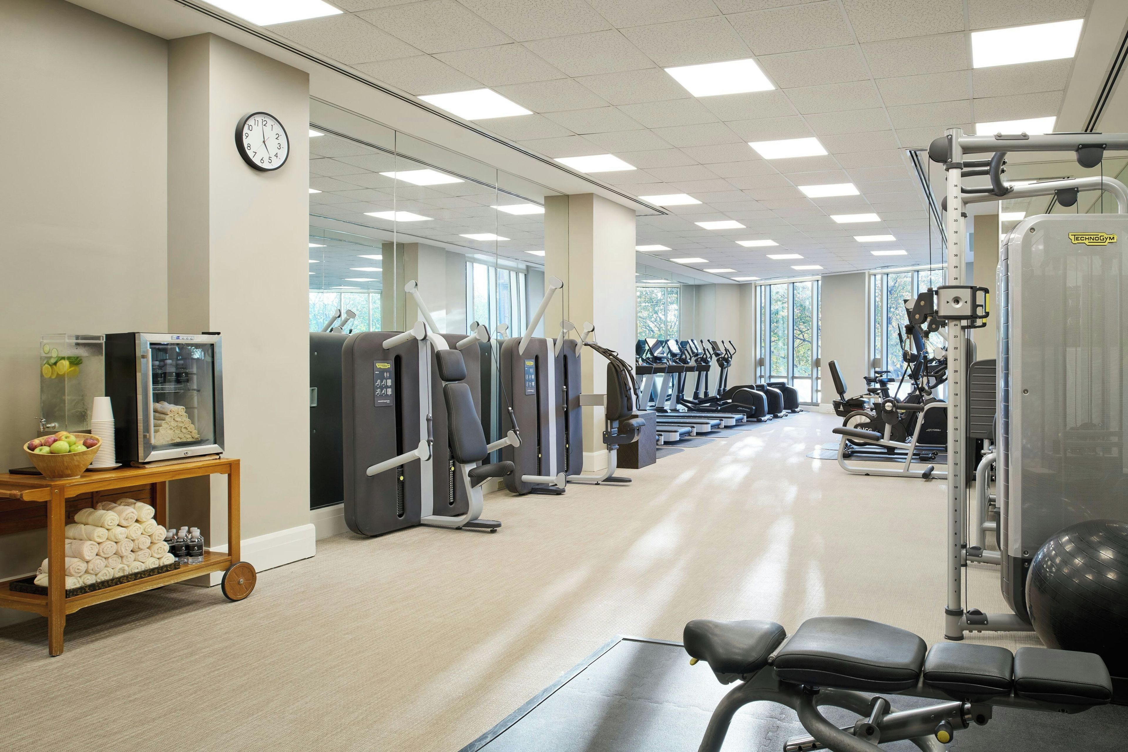 Een fitnessruimte met trainingsapparatuur, een klok en een waterdispenser.