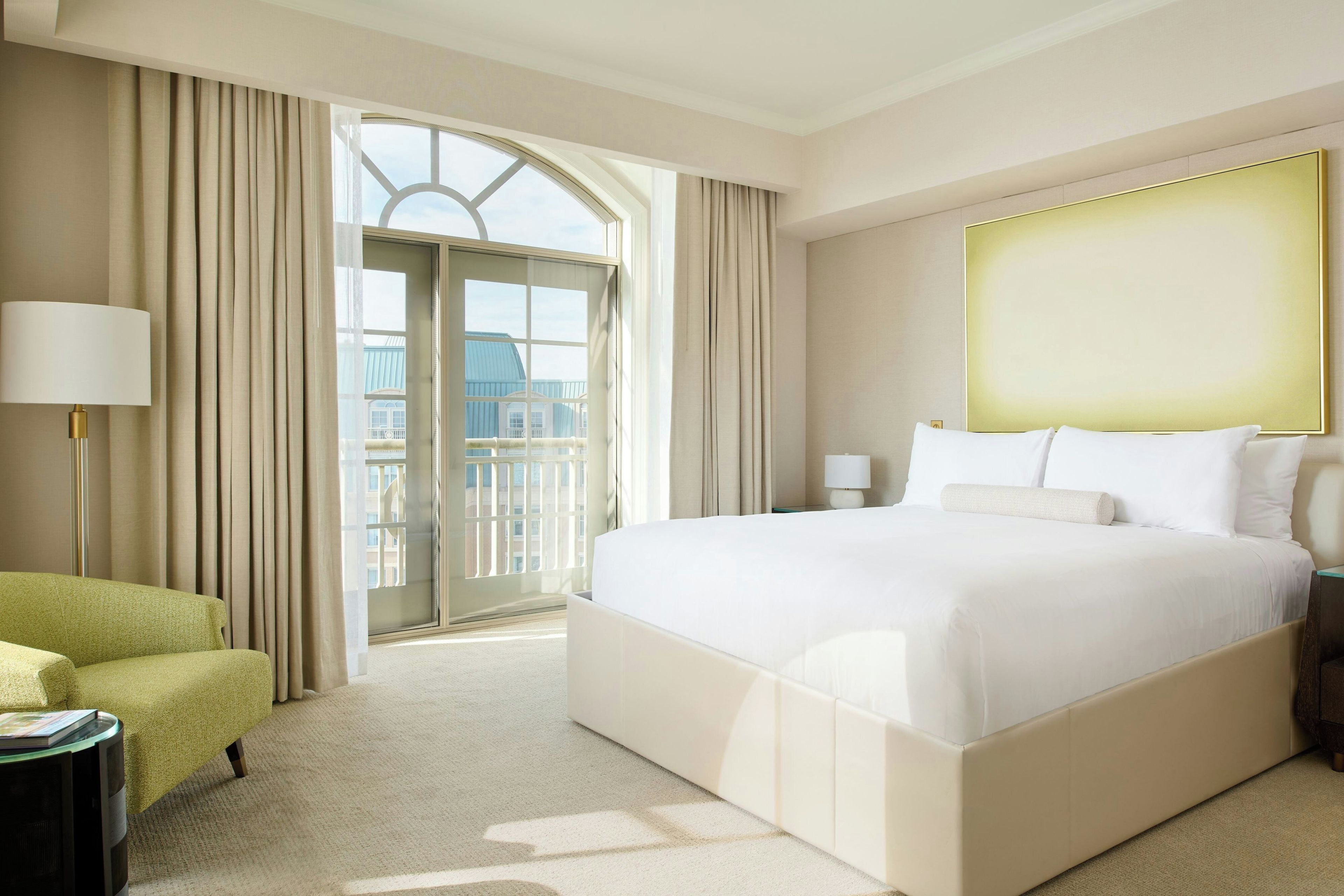 A hotel room with a large bed, a chair, a nightstand, and a view of the outside.