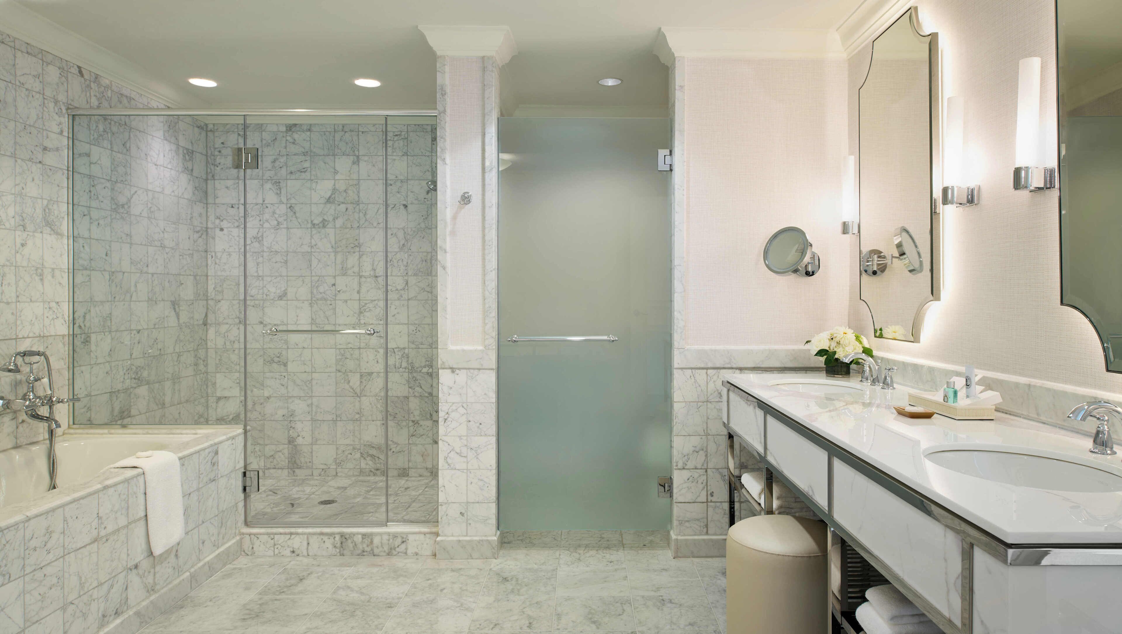 Un baño moderno con ducha envuelta en vidrio, un amplio lavamanos doble e iluminación integrada en el espejo.