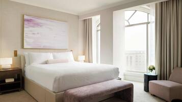 A modern hotel room with a large bed, a bench, a chair, a nightstand, a bedside table, and a window with curtains.