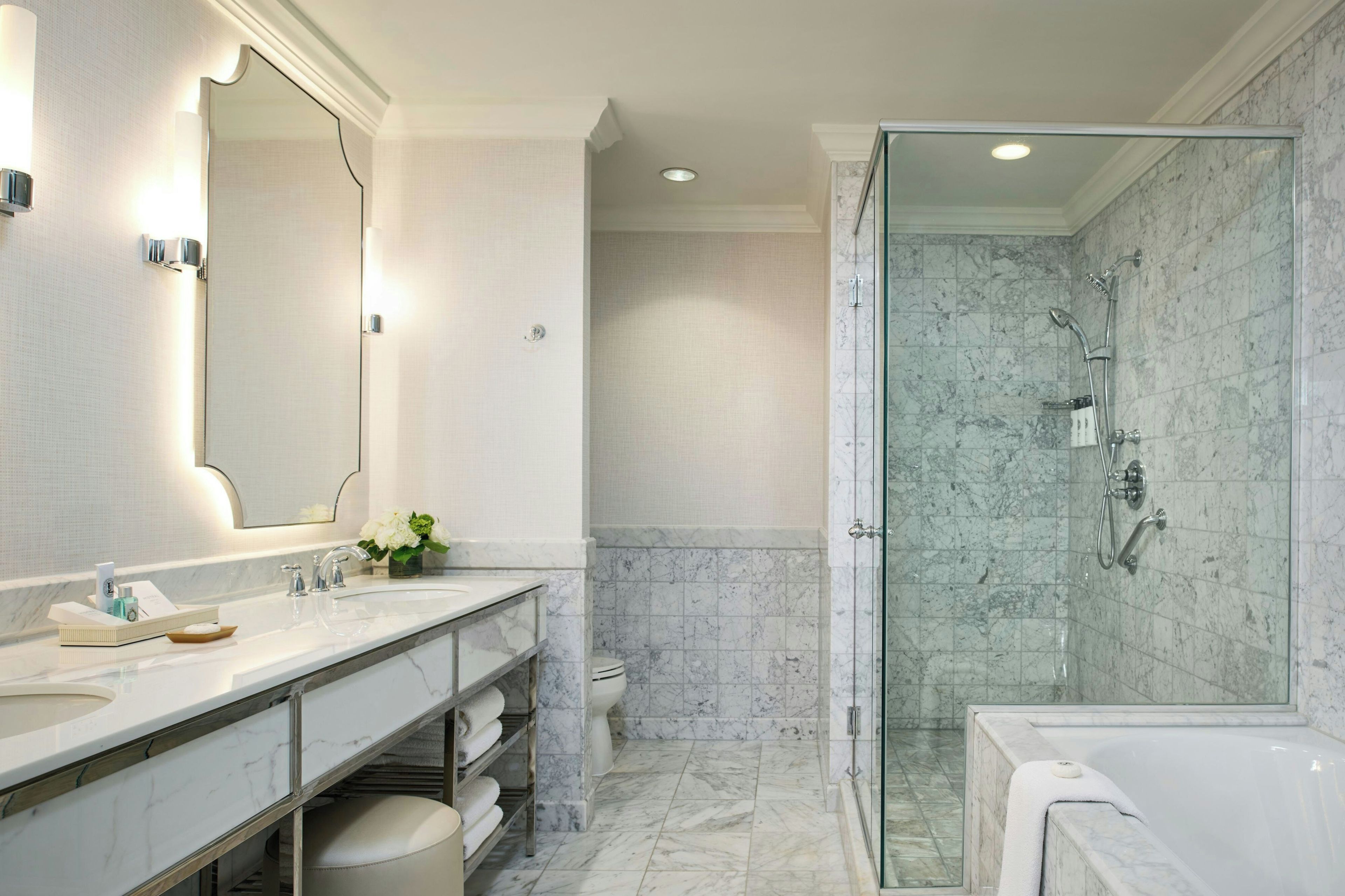 A modern bathroom with a glass-enclosed shower, a large mirror, and a vanity with a marble countertop.
