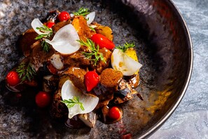 Un plato de carne asada con vegetales y hierbas en un recipiente de metal.