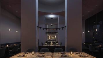 A modern dining area with a long table set for a meal, a kitchen in the background, and pendant lighting.
