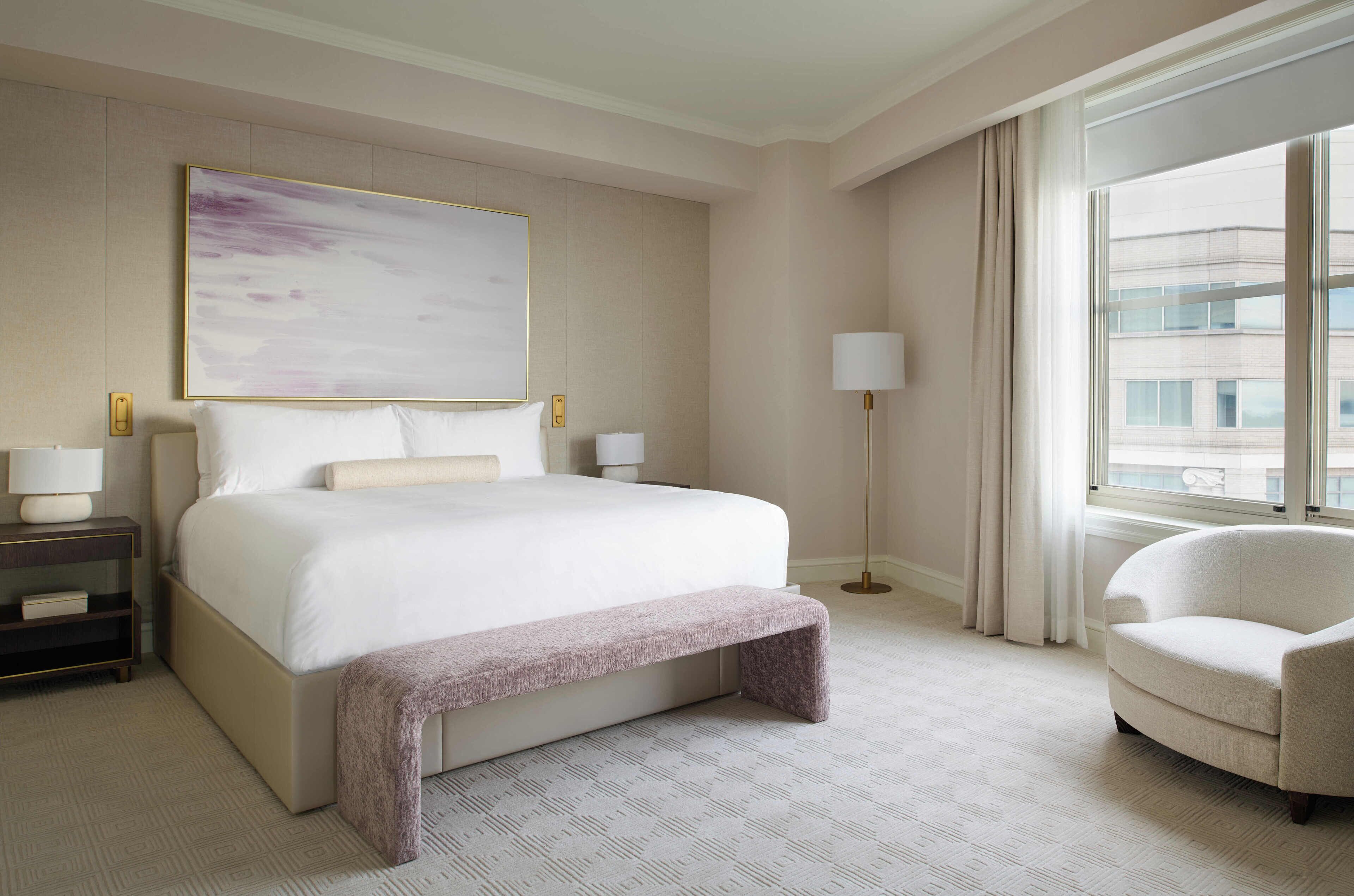 A hotel room with a large bed, bedside tables, a chair, a window with curtains, and a painting on the wall.