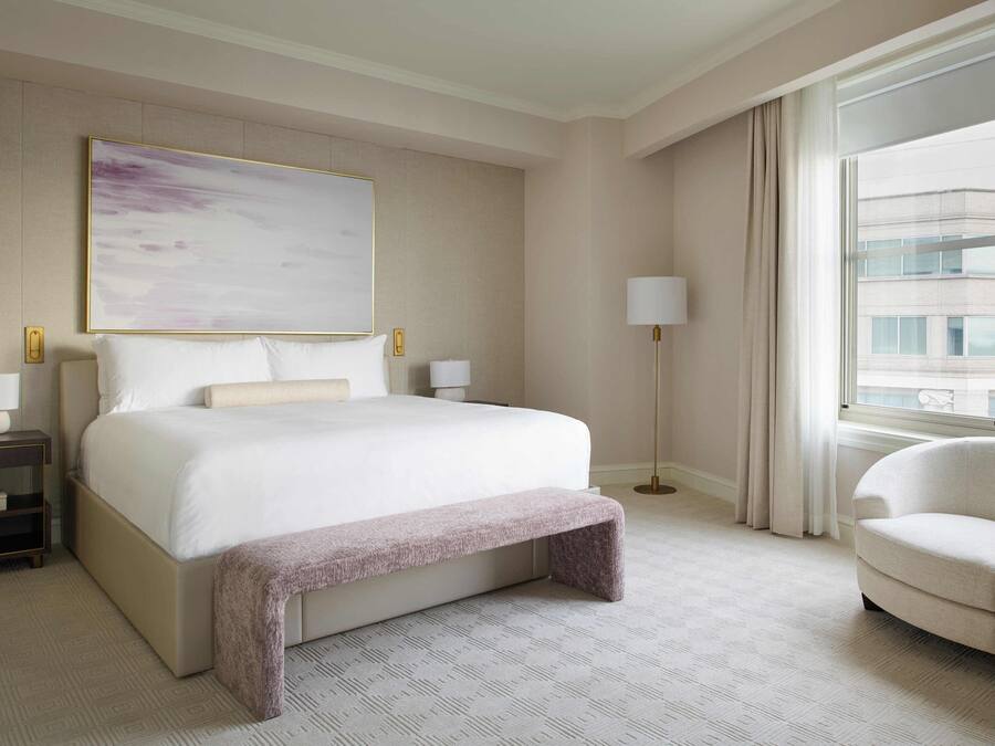 A hotel room with a large bed, bedside tables, a chair, a window with curtains, and a painting on the wall.
