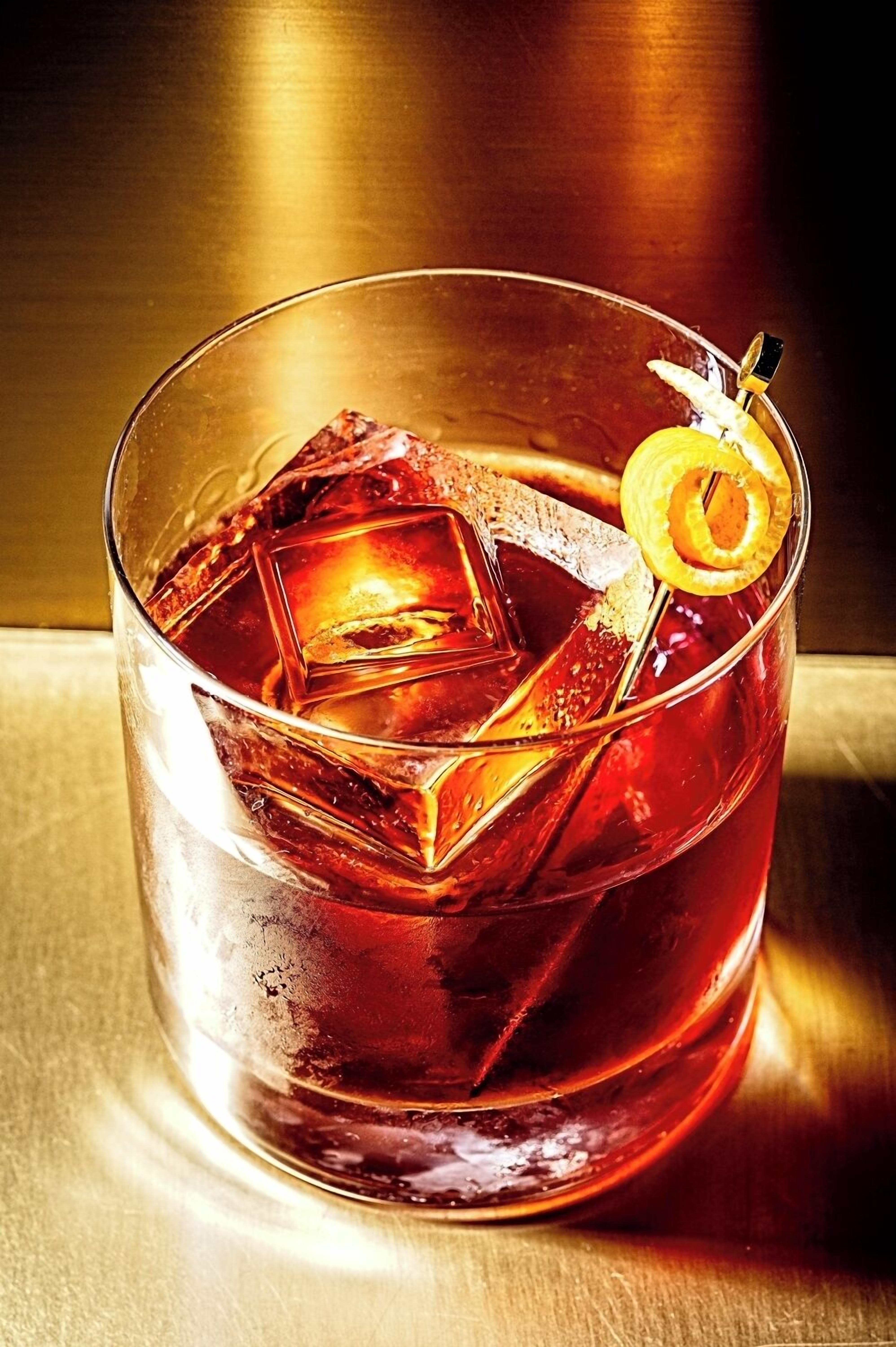 A clear glass with a dark amber liquid, ice cubes, and a lemon slice garnish.