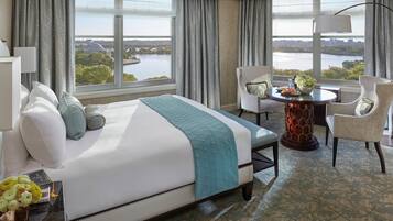 Een hotelkamer met een groot bed, een eettafel en uitzicht op water en een stadsbeeld.