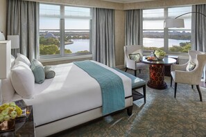 Habitación de hotel con una cama grande, una mesa de comedor y vistas a un cuerpo de agua y al paisaje urbano.
