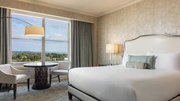 A hotel room with a large bed, two chairs, a round table, and a view of the outdoors.
