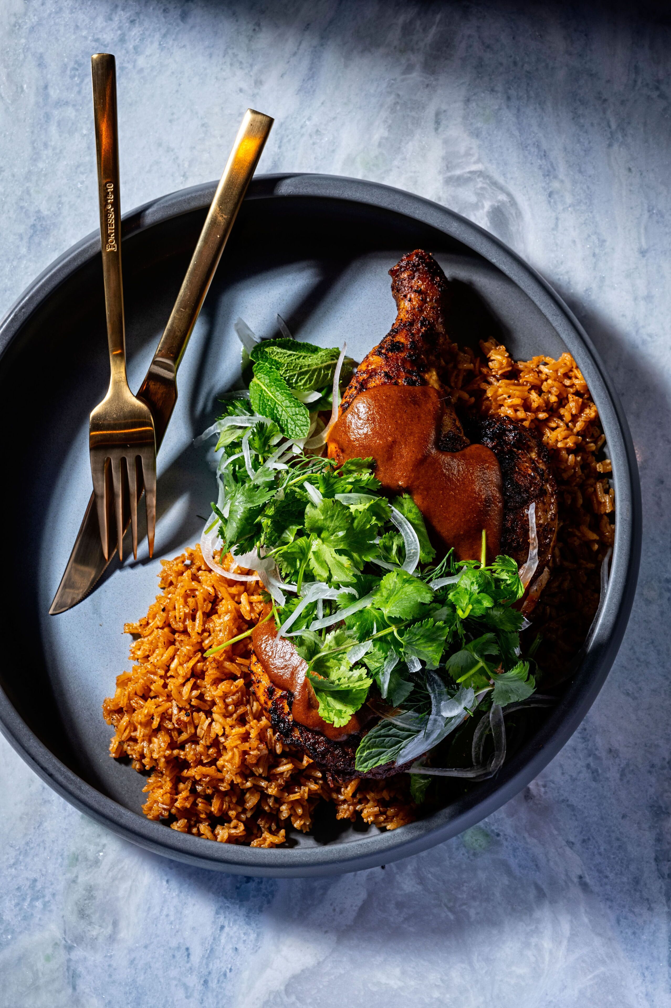 A plate of food with a roasted chicken leg, rice, and greens.