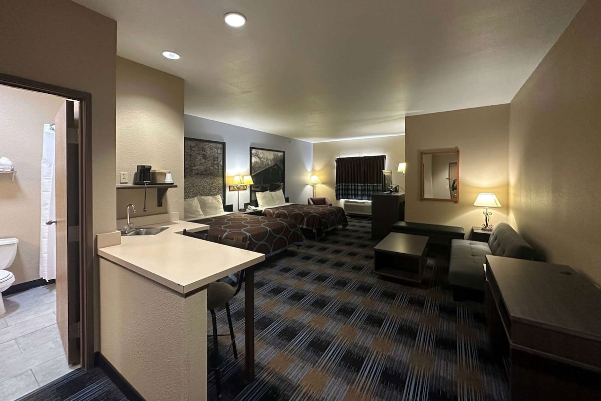 Une chambre d’hôtel comprenant un lit, un bureau, un canapé, une petite table, un miroir et une salle de bain visible à travers une porte ouverte.