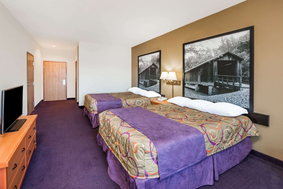 Une chambre d’hôtel avec deux lits, une télévision, une commode et deux lampes fixées au mur.