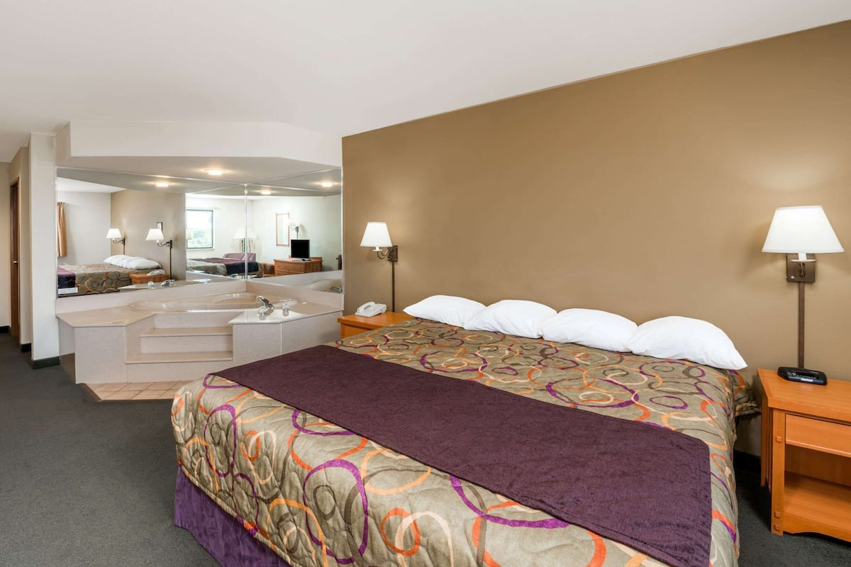 Une chambre d’hôtel avec un grand lit, une salle de bain séparée avec une baignoire et un miroir qui reflète la pièce.