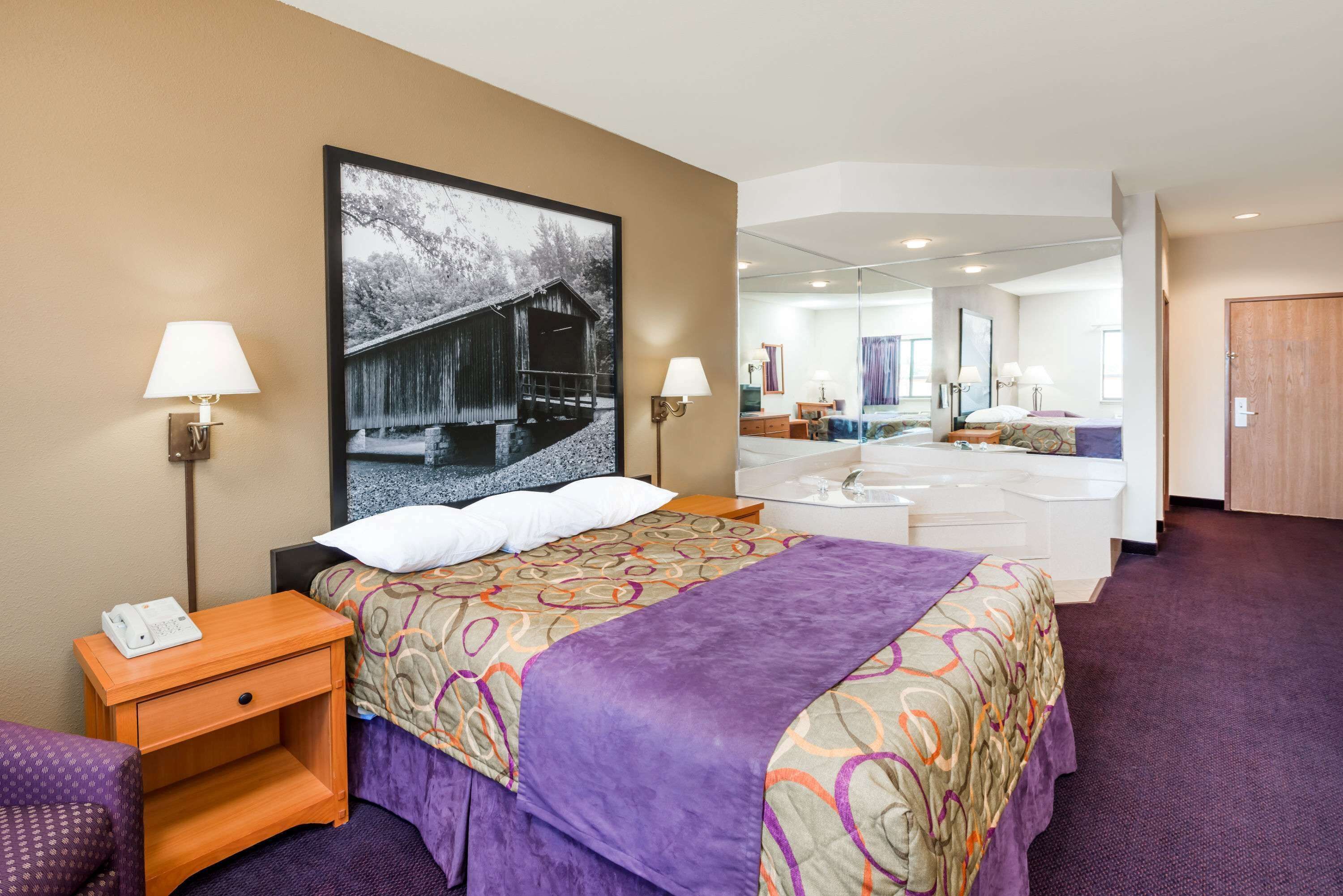 A hotel room with a bed, bedside tables, a desk, a mirror, a bathroom with a sink and mirror, and a large window.