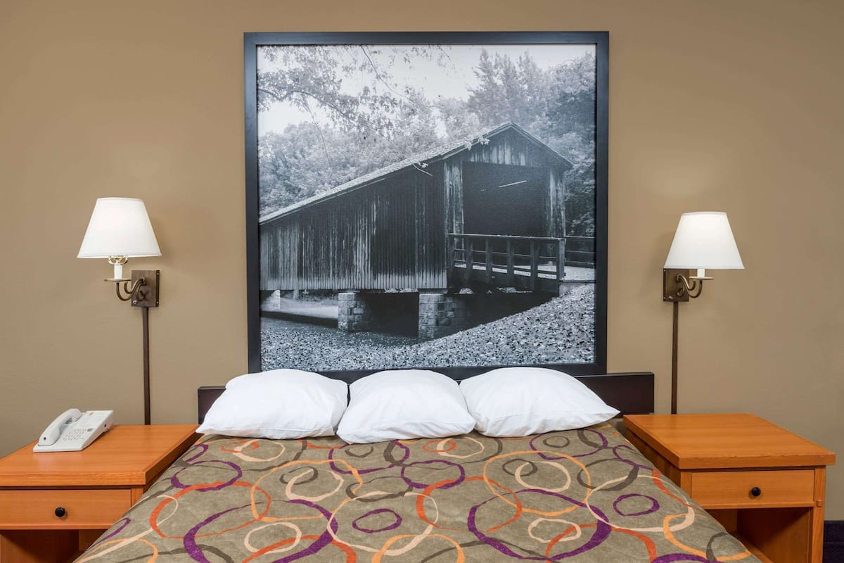 Une chambre d’hôtel avec un lit, deux tables de chevet, un téléphone et un tableau encadré au mur.