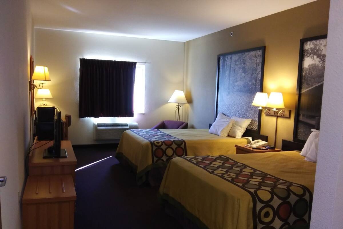 Une chambre d’hôtel avec deux lits, un bureau avec un ordinateur, une fenêtre avec des rideaux et un téléviseur fixé au mur.