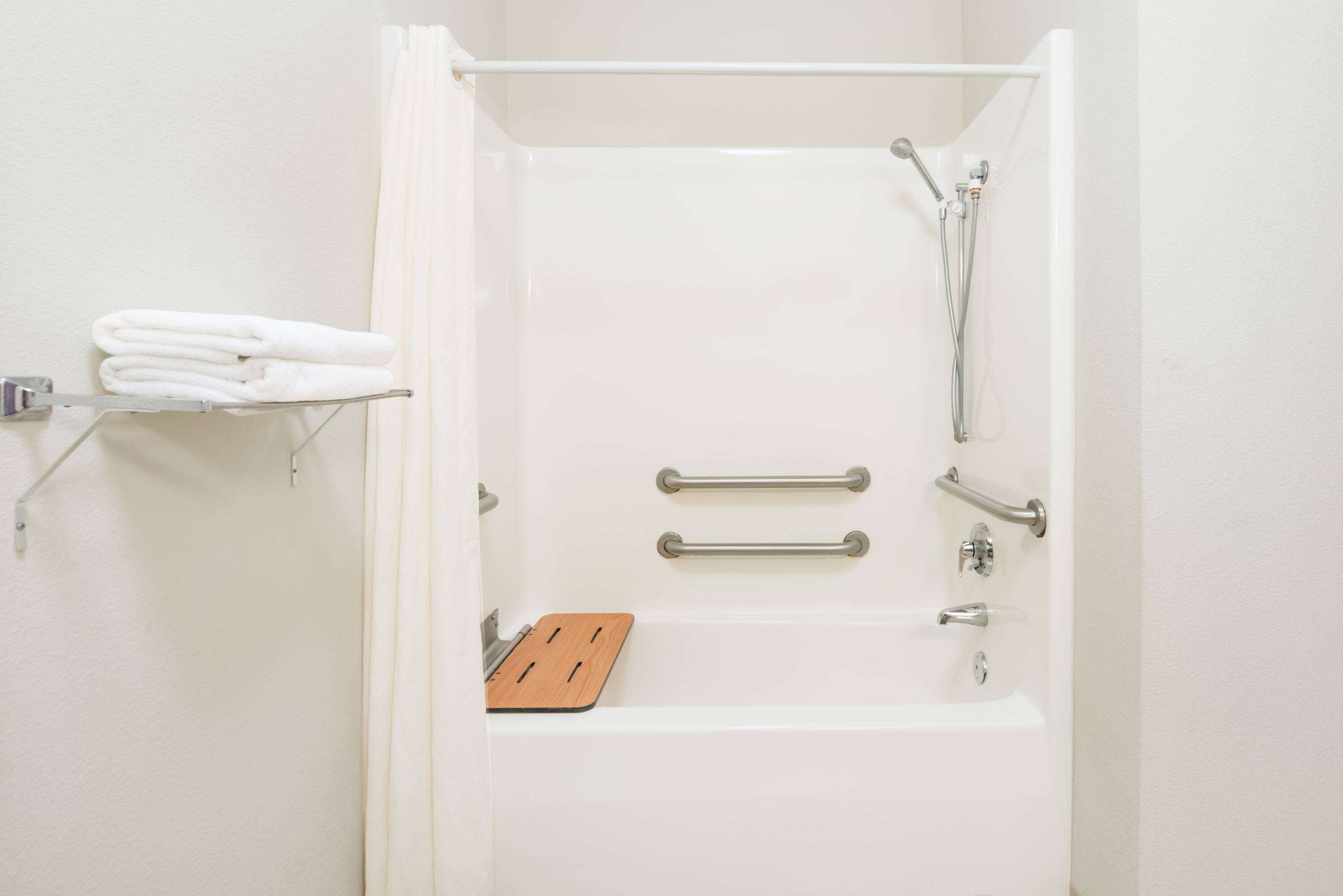 A white bathroom with a bathtub, grab bars, and a towel rack.
