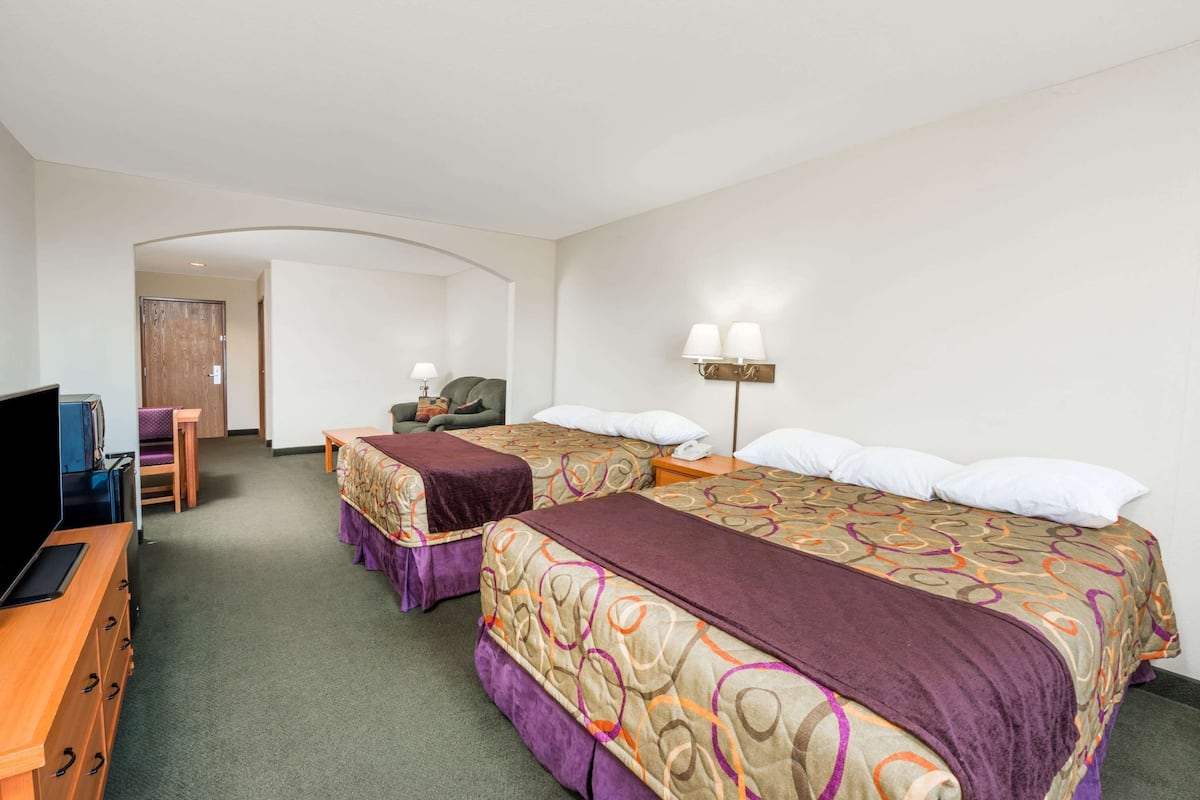 Une chambre d’hôtel avec deux lits, un bureau équipé d’une télévision et d’une lampe, et une porte donnant sur une autre pièce.