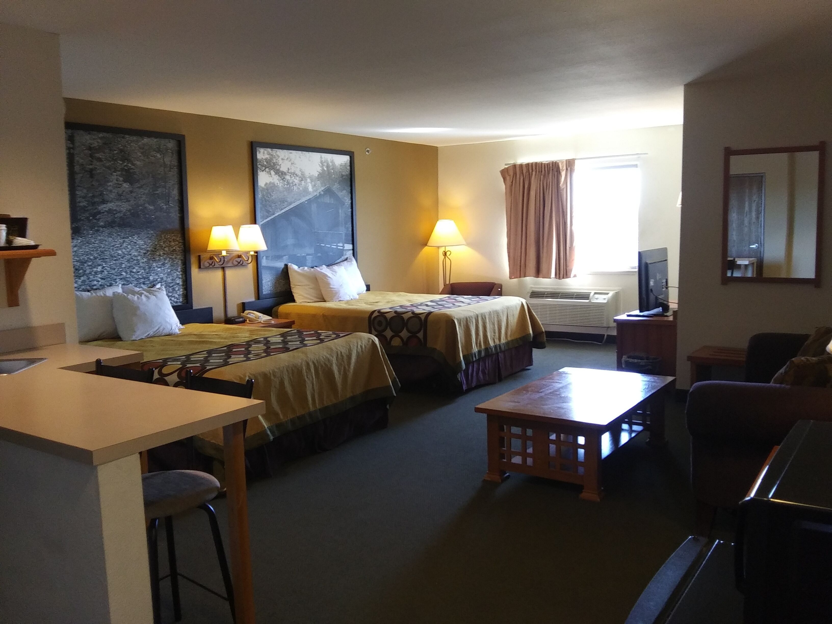 A hotel room with two beds, a desk, a chair, a TV, and a window with curtains.