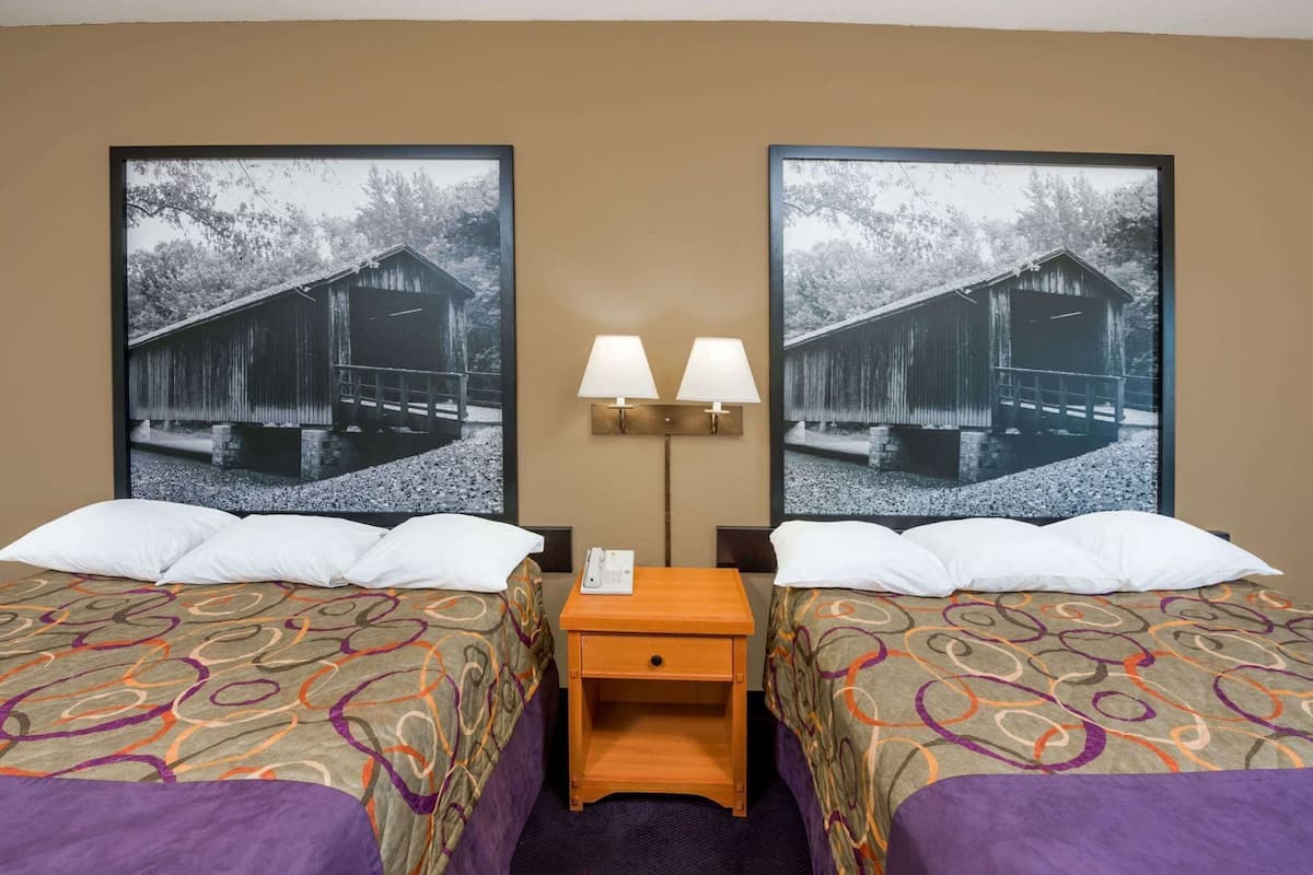 Une chambre d’hôtel avec deux lits, une table de chevet, une lampe et deux tableaux représentant une structure en bois.