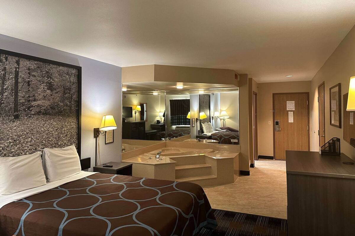 Une chambre d’hôtel avec un lit, un grand miroir, une salle de bain avec une baignoire et un bureau.