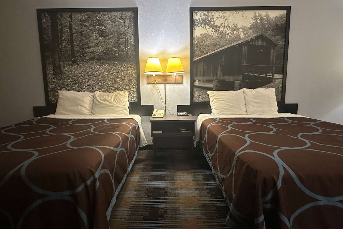 Une chambre d’hôtel avec deux lits, une table de chevet avec une lampe et un grand tableau encadré au mur.