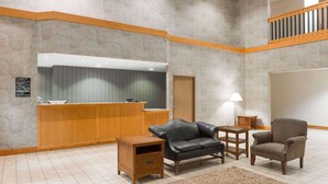 A lobby with a reception desk, leather sofa, armchair, wooden side table, and a small rug.