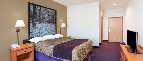 A hotel room with a bed, two bedside lamps, a TV on a wooden dresser, and a large framed picture on the wall.