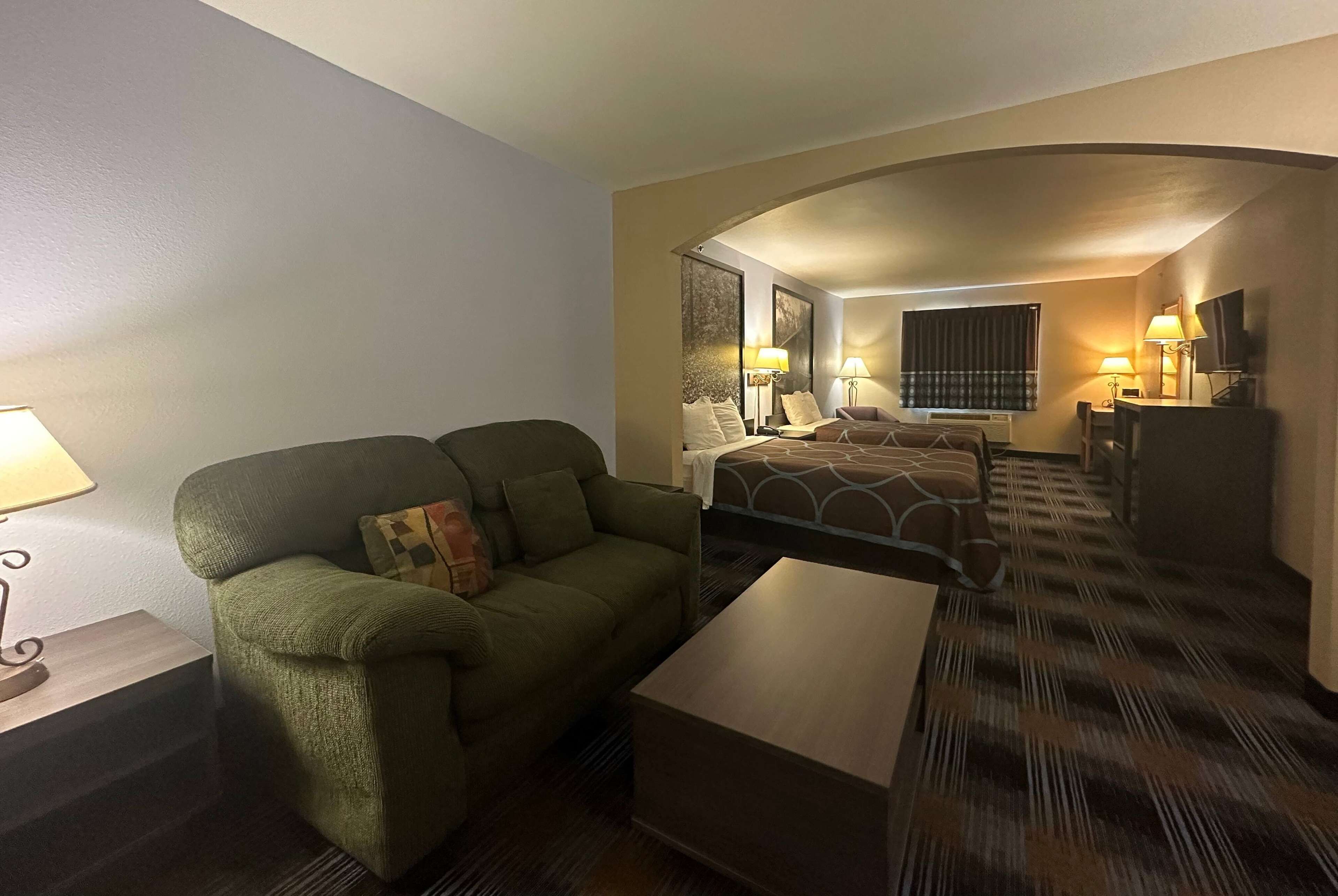 Quarto de hotel com sofá verde, cama com colcha estampada, uma mesinha e duas luminárias de cabeceira.