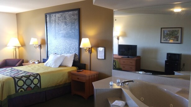 A hotel room with a bed, two bedside lamps, a nightstand, a TV, a mirror, a bathroom with a bathtub, and a large painting on the wall.
